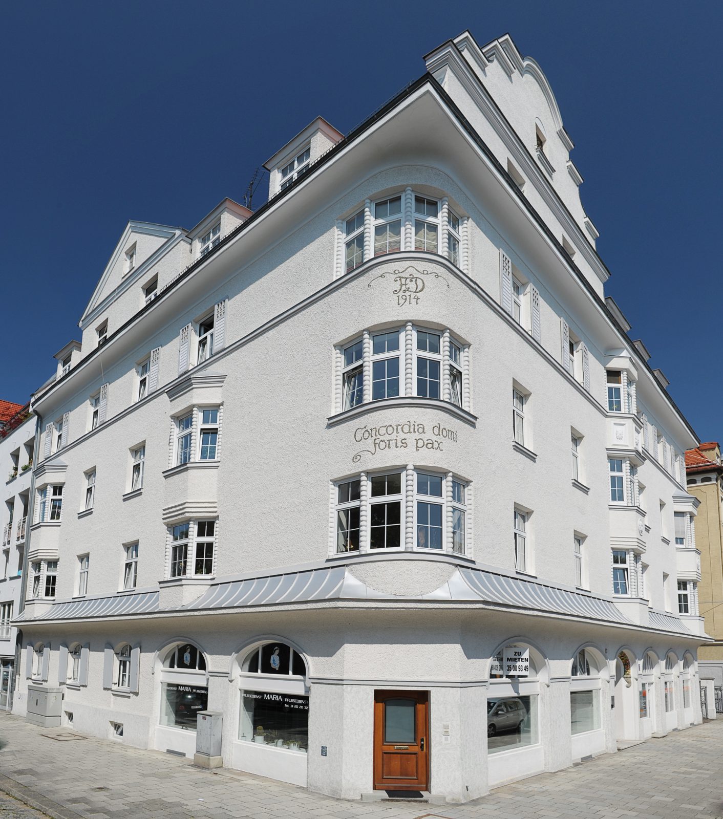 Weißes Jugendstil-Eckhaus von 1914 mit Erkern vor tiefblauem Himmel