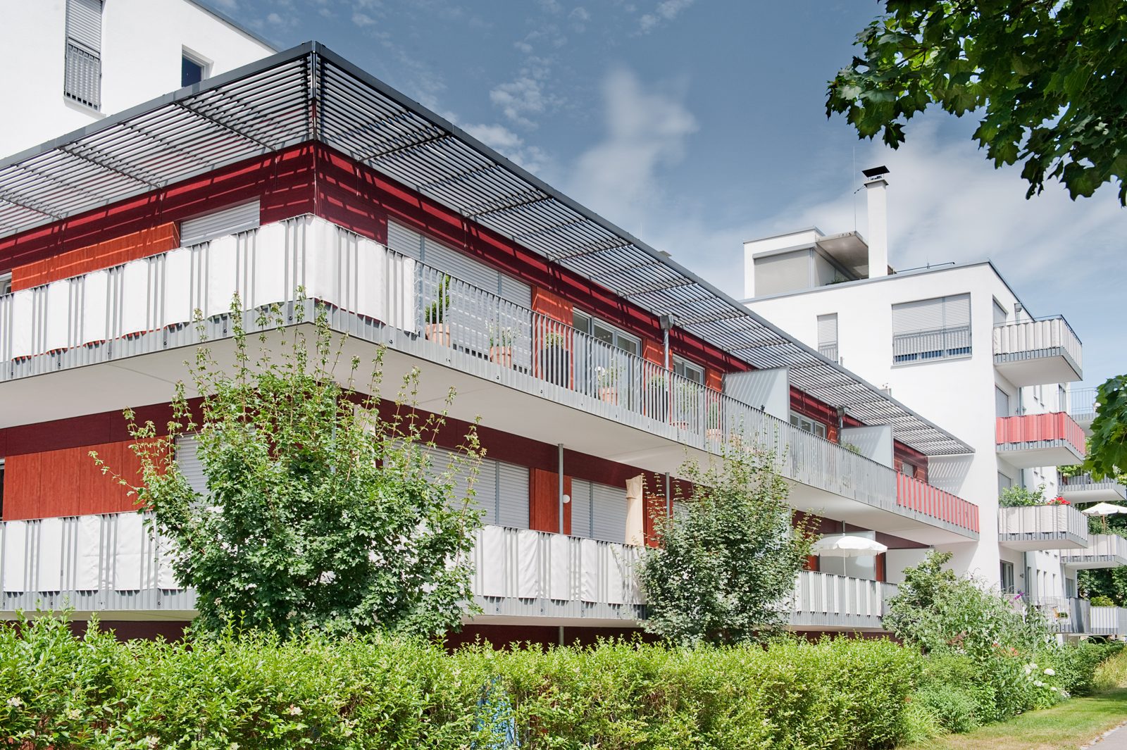 Moderne Wohnanlage mit roter Fassade, Balkonen und Grünanlage
